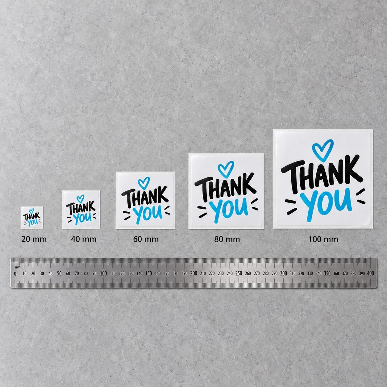 Square thank-you stickers at 20, 40, 60, 80 and 100 mm above a steel ruler